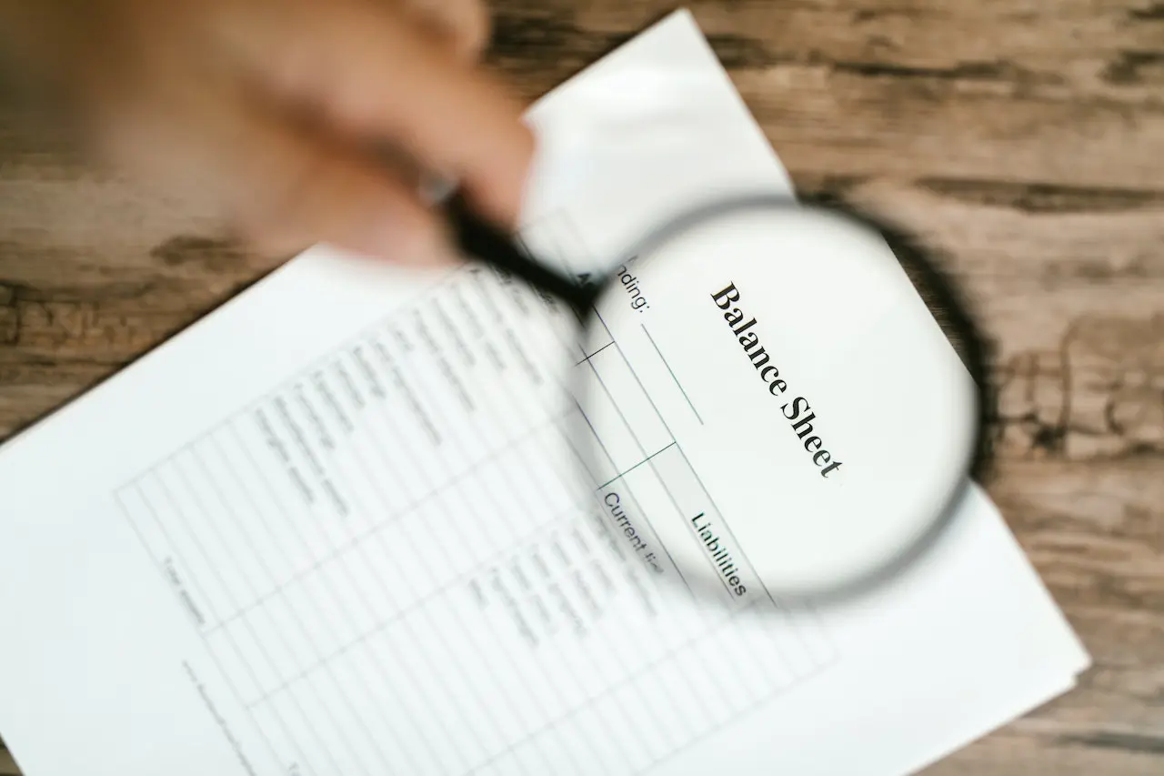 man using a magnifying glass to read balance sheet